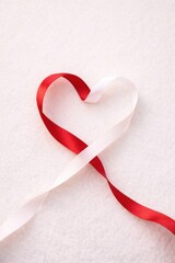 Red and white satin ribbons shaped into a heart on a soft white textured background. Minimalist romantic concept for Valentine's Day, wedding invitation, or love symbol. Top view with copy space.