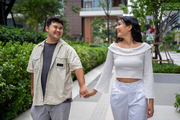 Portraying contemporary consumerism, two young Asian ladies walk side-by-side in an open-air mall setting. They carry multiple bags containing merchandise and appear content with their acquired goods.