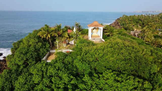 Aerial drone footage of Unawatuna Beach in Sri Lanka with traditional fishing boats on the shore and a Buddhist temple near the coastline. Tropical ocean, sandy beach and cultural landmarks.