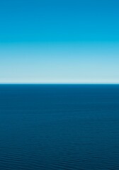Fototapeta premium Minimalist abstract background featuring a razor-sharp horizon line separating the endless blue sky from the deep ocean water, clean, peace, bright