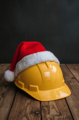 Yellow construction helmet with Santa hat on wooden table festive safety concept