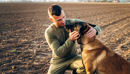 Military soldier handler kneeling and petting K9 working dog in field at sunset for bonding concepts
