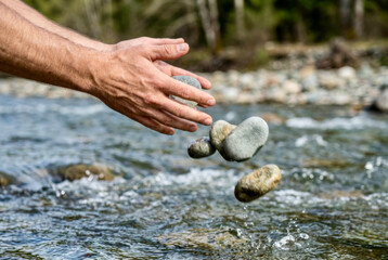 Hands toss stones into a river during a sunny afternoon by the water&rsquo;s edge in a natural setting