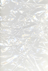 Abstract crumpled plastic texture with glowing light reflections creating a metallic and futuristic effect. Shiny surface and intricate folds form abstract background for modern design concepts.