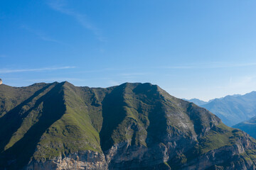Fototapeta premium Distinctive green mountain ridges rise steeply above rocky cliffs in the Pyrenees near Gavarnie Gedre. Bright sunlight and crisp shadows highlight the rugged alpine terrain and open sky.