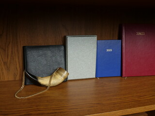Notebooks and planners from different years on wooden shelf with decorative horn in calm composition.