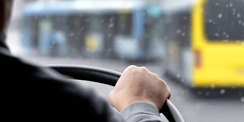 Bus driver holding steering wheel, navigating traffic and blurring city streets in light snowfall