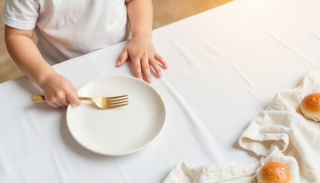 Young child holding fork over empty plate on dining table  