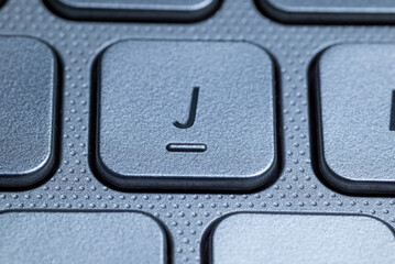 Close-up macro view of the "J" key on a gray laptop keyboard with detailed texture and selective focus.