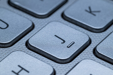 Close-up macro view of the "J" key on a gray laptop keyboard with detailed texture and selective focus.
