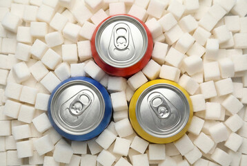 Top view of colorful aluminum soda cans surrounded by white sugar cubes, representing high sugar content in soft drinks