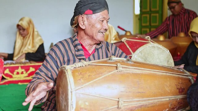 Elderly Javanese musician playing a traditional gamelan kendang drum