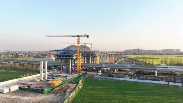 High-speed railway station under construction with cranes surrounded by farmland and green fields