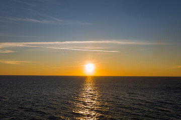 Obraz premium The sun sets low above the calm Ionian Sea, casting a luminous golden reflection across gentle waves. Subtle cloud streaks and a gradient sky create a tranquil, minimal seascape.