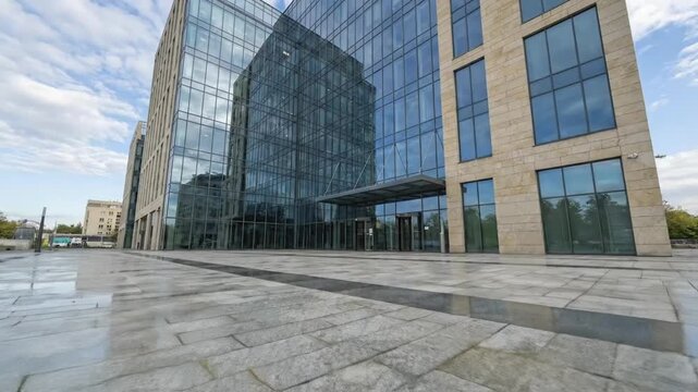 A dynamic wide-angle shot showcases a sleek, modern corporate building with an impressive facade combining reflective blue-tinted glass panels and elegant light-colored stone cladding. The contemporar