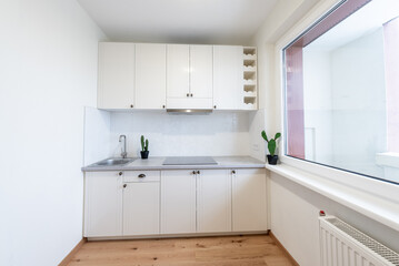 Fototapeta premium Modern White Kitchen Interior with Large Window and Wooden Flooring