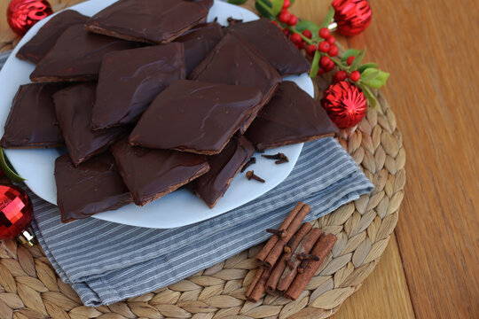 Italian traditional festive cookies called Mostaccioli or Mustaccioli on a plate on wooden table with Christmas decorations and holly. Christmas cookies made mith Pisto, a mix of various spices