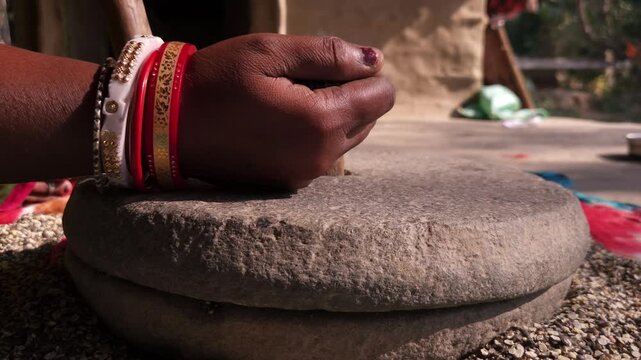 Indian woman in a rural village uses a traditional hand operated millstone (quern) to grind black gram lentils, showcasing authentic village life, heritage food preparation, and indigenous household
