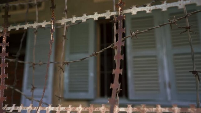 Windowed prison barbed wire rusting around building at Tuol Sleng showing barred openings and preserved detention structure, Khmer Rouge Genocide