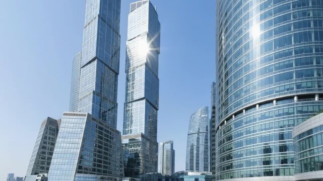 A stunning low-angle shot captures the majestic grandeur of modern skyscrapers reaching towards a clear blue sky. Sleek, contemporary glass facades reflect the brilliant sunlight, creating dynamic pat