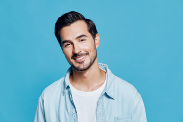 Smiling man wearing light blue shirt poses against a bright blue background, exuding a cheerful and friendly vibe with a charming expression. Portrait style.