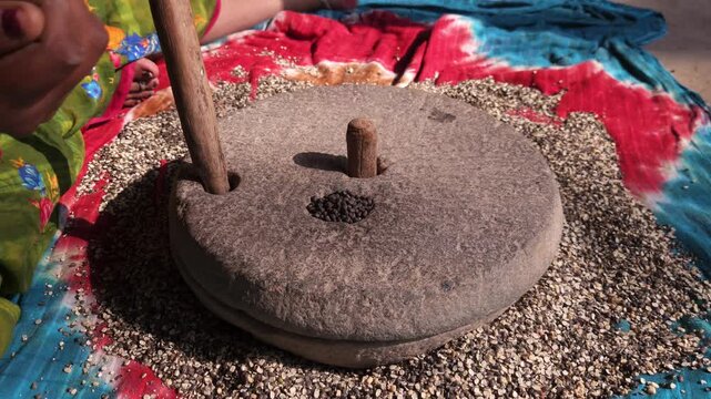 Indian woman in a rural village uses a traditional hand operated millstone (quern) to grind black gram lentils, showcasing authentic village life, heritage food preparation, and indigenous household