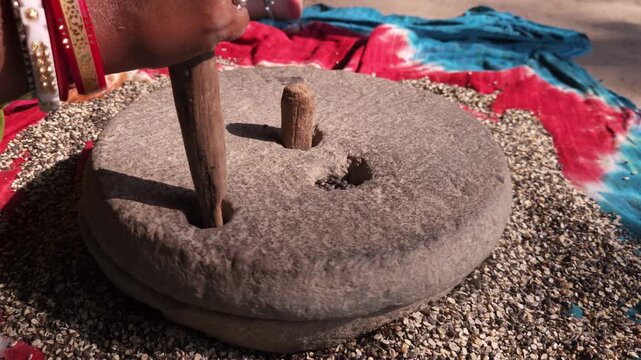 Indian woman in a rural village uses a traditional hand operated millstone (quern) to grind black gram lentils, showcasing authentic village life, heritage food preparation, and indigenous household