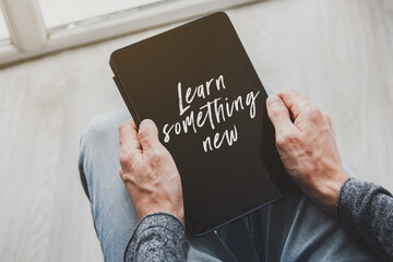Hands holding tablet with learn something new text on screen education motivation self improvement online learning and personal growth concept