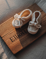 Fototapeta premium Baby name Elliott engraved on a wooden plaque with knitted baby shoes. Image for baby name reveal