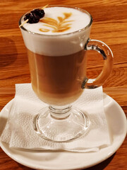 Latte coffee with milk foam art and pine cone garnish in glass.