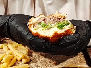 Hands in black gloves holding a juicy bitten burger.