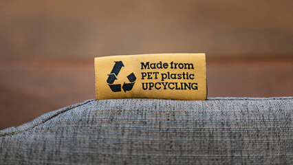 "PET Plastic upcycling" product label tag on the sofa seat fabric material part. Sign and symbol object photo, selective focus.