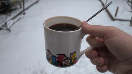 Hand holding a cup of hot coffee outdoors in winter, cozy moment with warm drink against snowy garden background, simple lifestyle scene showing comfort, cold weather, and calm everyday mood.