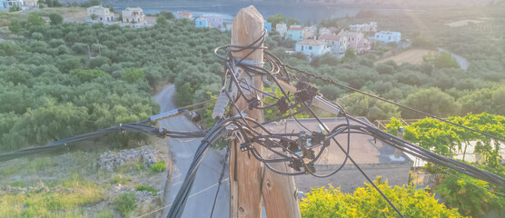 Web of wires on wooden pole with Cretan nature background, old electricity supply system