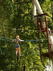 Yaslo, Poland - 8 7 2019:A young girl climbs the trees in gear in a park for rock climbing. Scandinavian attraction for sports events. Rope insurance and means of protection. Safety at altitude