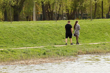 A young guy and his girlfriend are walking in the park along the lake shore. A walk of lovers in the fresh air on a day off. Family leisure in nature