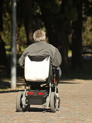 A woman is walking in the park with a man who is traveling on an electric wheelchair. Custody of the needy. The activity of people with limited mobility. Prosthetics of patients of the musculoskeletal