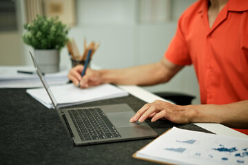 Working on laptop computer and writing on document paper, multitasking