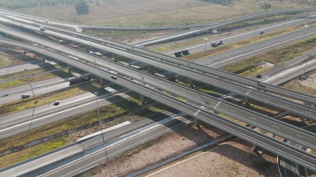 Aerial view of modern highway interchange with multilayer roads and curved ramps surrounded by green farmland, showcasing transportation infrastructure, urban development, and road network planning.