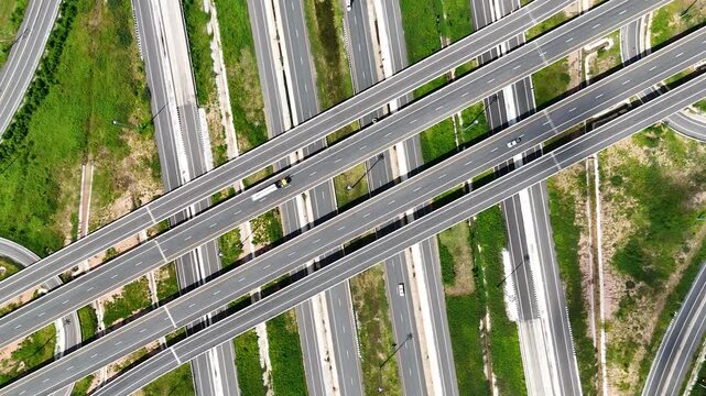 Aerial view of modern highway interchange with multilayer roads and curved ramps surrounded by green farmland, showcasing transportation infrastructure, urban development, and road network planning.