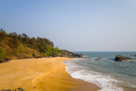 Expansive golden sand beach meets gentle waves and rugged rocks along the tranquil coastline of Bekal, India. Warm sunlight highlights the natural textures and peaceful atmosphere.