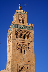 Fototapeta premium Koutoubia-Moschee in Marrakesch: Das markante Minarett aus rötlichem Sandstein erhebt sich vor tiefblauem Himmel über die historische Altstadt. 