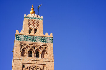 Fototapeta premium Koutoubia-Moschee in Marrakesch: Das markante Minarett aus rötlichem Sandstein erhebt sich vor tiefblauem Himmel über die historische Altstadt. 