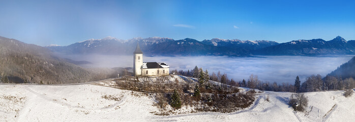 Mystical Panorama of Saint Thomas Church in Slovenia: Alpine Chapel in Transparent Mist and golden Morning Sunlight. winter scenery