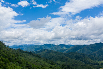 Fototapeta premium Vast forested hills and layered mountain ridges stretch beneath a brilliant blue sky filled with textured clouds in the rural region between Phonsavan and Phou Khoun, Laos. The landscape highlights