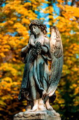 Historische Farbaufnahme eines betenden und trauerndem Friedhofsengel auf einem Grab mit unscharfem, gelb verf&auml;rbtem Herbstlaub im Hintergrund
