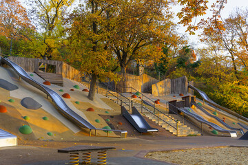 Colorful outdoor playground with climbing areas and modern design on a spring afternoon. Amazing fall-colored trees on the background