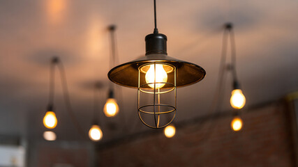 A classic style ceiling lighting lamp with iron cage during it glowing in warmlight shade. Interior object, close-up with selective focus.