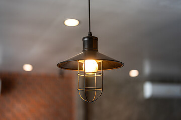 A classic style ceiling lighting lamp with iron cage during it glowing in warmlight shade. Interior object, close-up with selective focus.