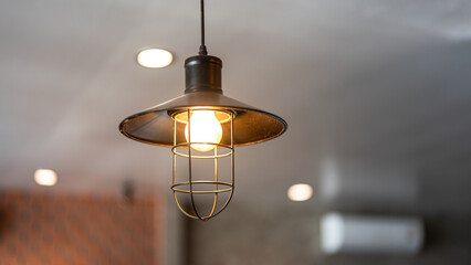 A classic style ceiling lighting lamp with iron cage during it glowing in warmlight shade. Interior object, close-up with selective focus.